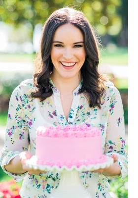 lindsay holding a pink cake on a cream colored cake stand