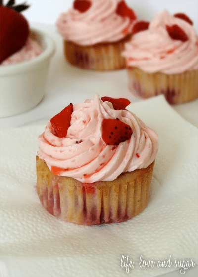 A strawberry Cupcake topped with icing and strawberries on a paper towel