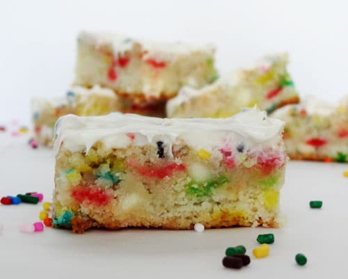 A square of Funfetti Cake Batter Blondie with Rainbow Chip Icing on top and sprinkles around it