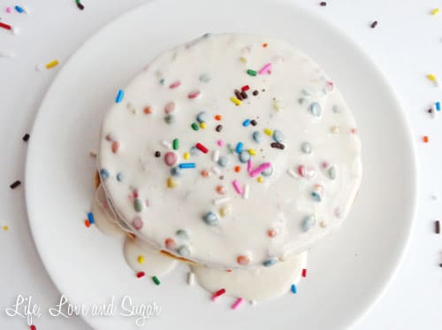 Top view of a stack of Funfetti Cake Batter Pancakes with Rainbow Chip Icing Syrup on a white plate