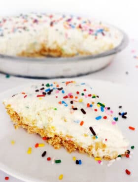 A slice of Funfetti Cake Batter Ice Cream Pie on a white plate with sprinkles