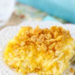 One serving of a cheesy hashbrown casserole on a white plate with fancy cutouts on the rim