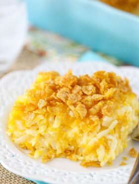 One serving of a cheesy hashbrown casserole on a white plate with fancy cutouts on the rim