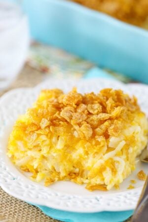 One serving of a cheesy hashbrown casserole on a white plate with fancy cutouts on the rim