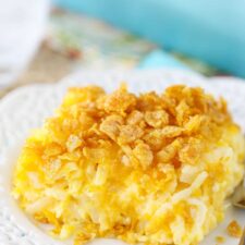 A serving of cheesy hashbrown casserole with a crushed cornflake topping on a plate.