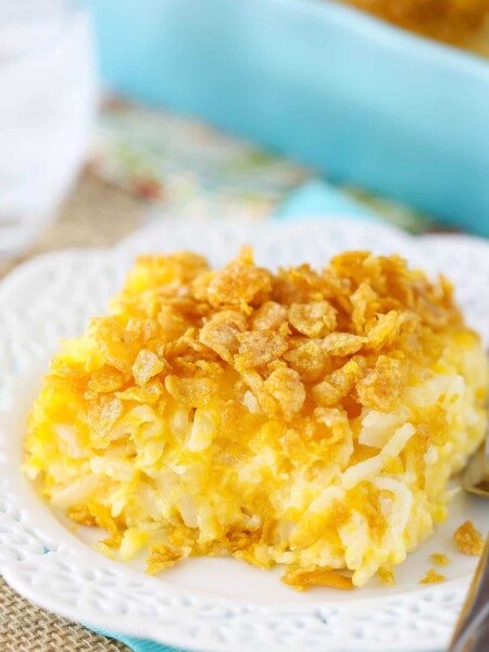A serving of cheesy hashbrown casserole with a crushed cornflake topping on a plate.