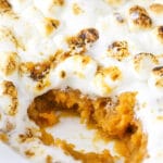 A warm sweet potato casserole topped with gooey toasted marshmallows inside of a white baking dish