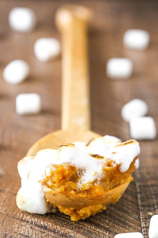 A bite of sweet potato casserole on a spoon with mini marshmallows in the background.