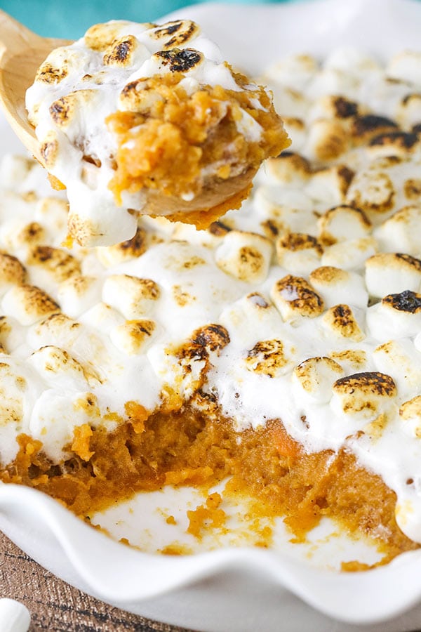 A freshly baked sweet potato casserole in a baking dish with a wooden spoon scooping some out