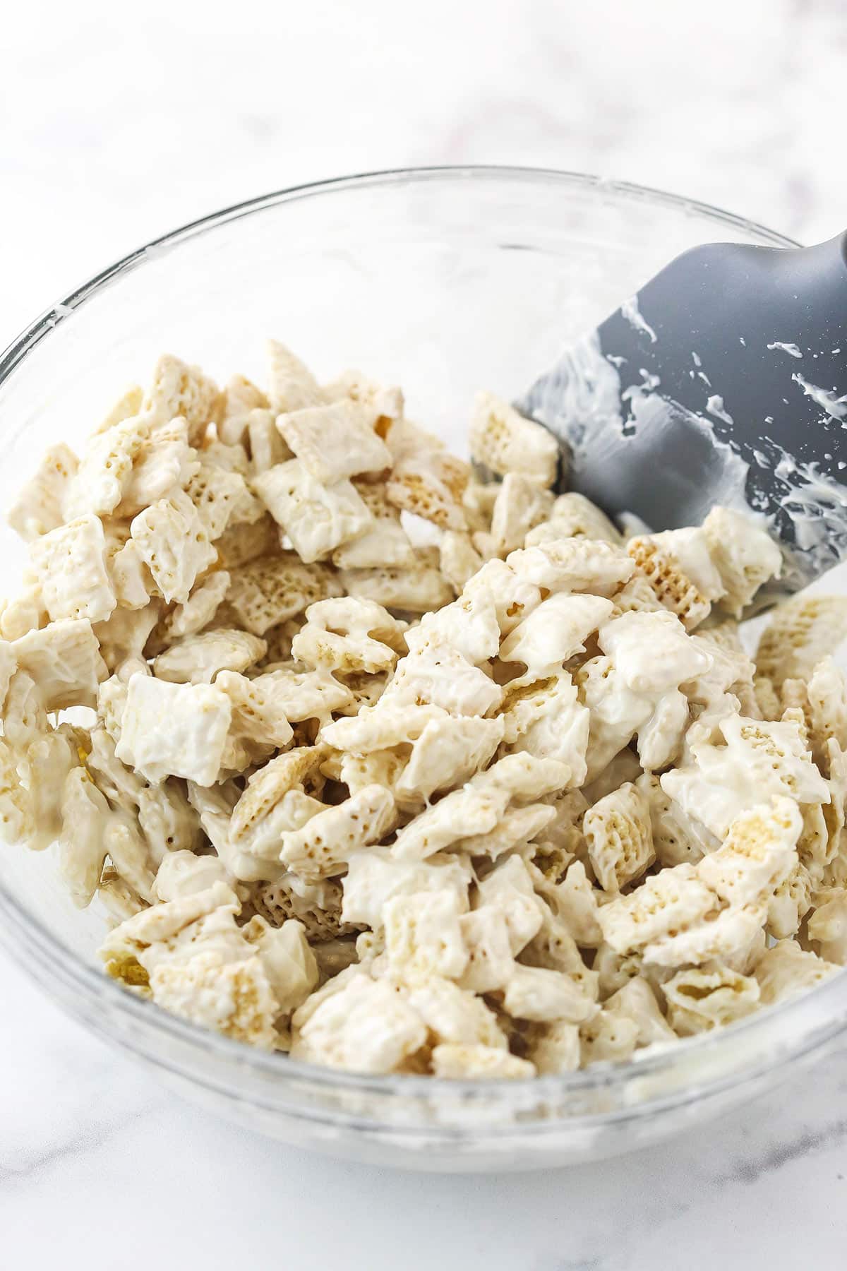 rice chex cereal being stirred with white chocolate in glass bowl