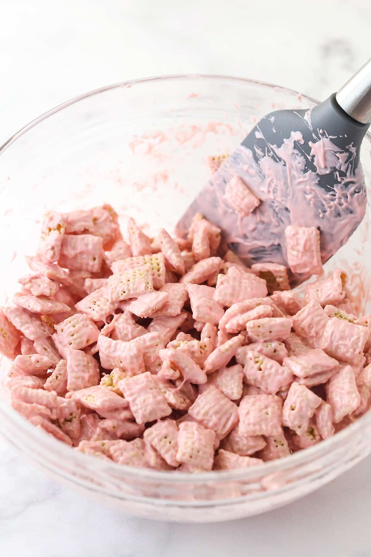 pink melting chocolate being stirred with the rice chex cereal in glass bowl