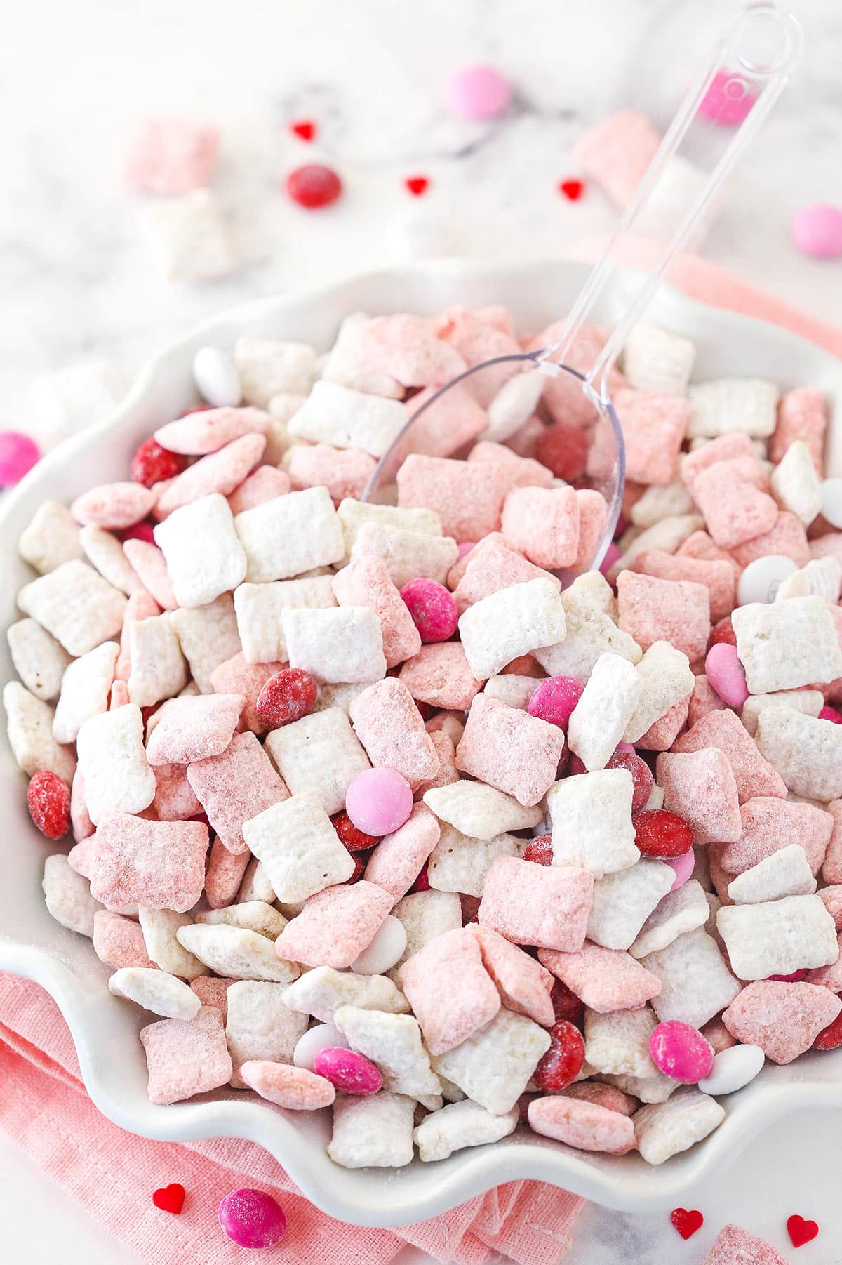 pink and white strawberries and cream puppy chow in white ruffle bowl with clear scoop