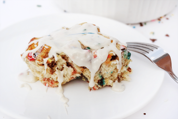 A piece of Funfetti Cinnamon Roll Casserole with a bite missing and a fork nearby 