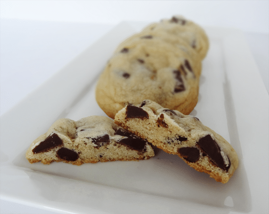 Four New York Times Cookies on a White Plate with the Front Cookie Split in Two Halves