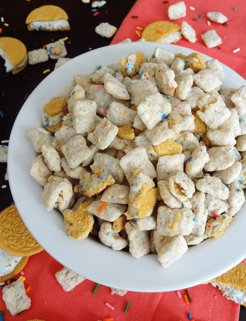 Golden Birthday Cake Oreo Puppy Chow in a white bowl surrounded by more Oreos and sprinkles 