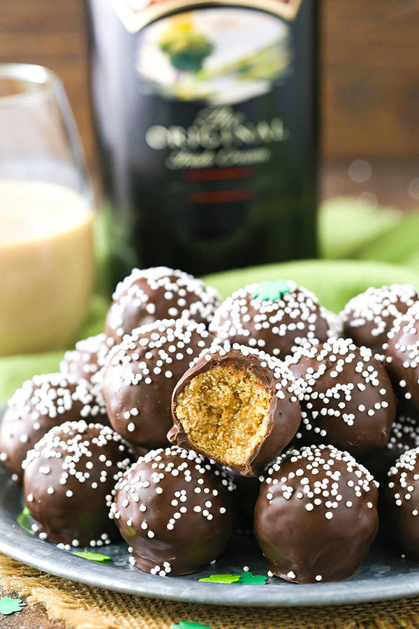 A pile of Irish Cream cookie balls on a plate with a bottle of Baileys in the background