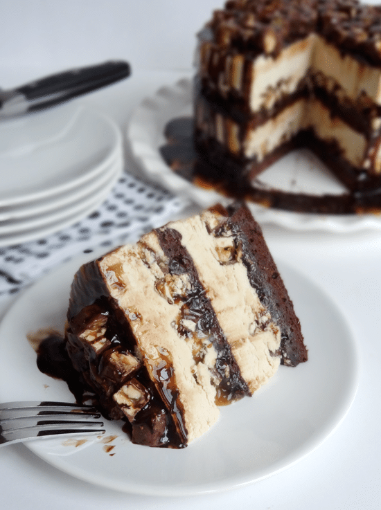 A Slice of Snickers Cake on a White Plate in Front of a Stack of Other Plates