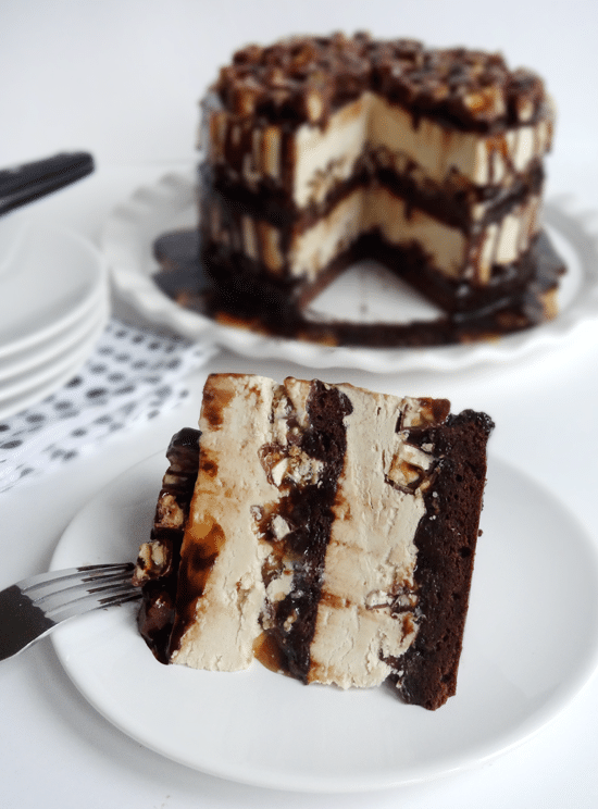 A Slice of Snickers Ice Cream Cake on a Plate with the Rest of the Cake in the Background