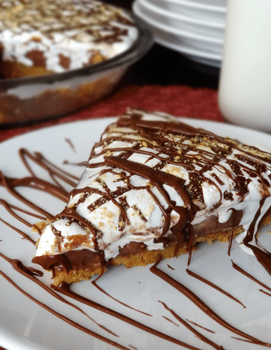 Close up of a a slice of Nutella, Peanut Butter and Marshmallow Pie on a white plate with chocolate drizzle 