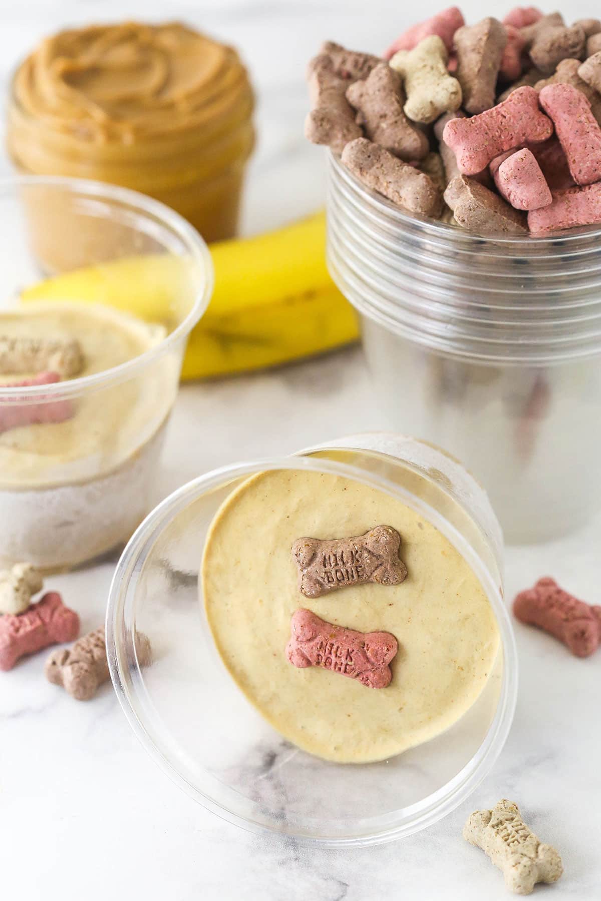 These Peanut Butter Banana Frozen Dog Treats are made with 2 ingredients in less than 5 minutes. The perfect summer doggy treat! Frozen dog treats in plastic cups topped with little bones