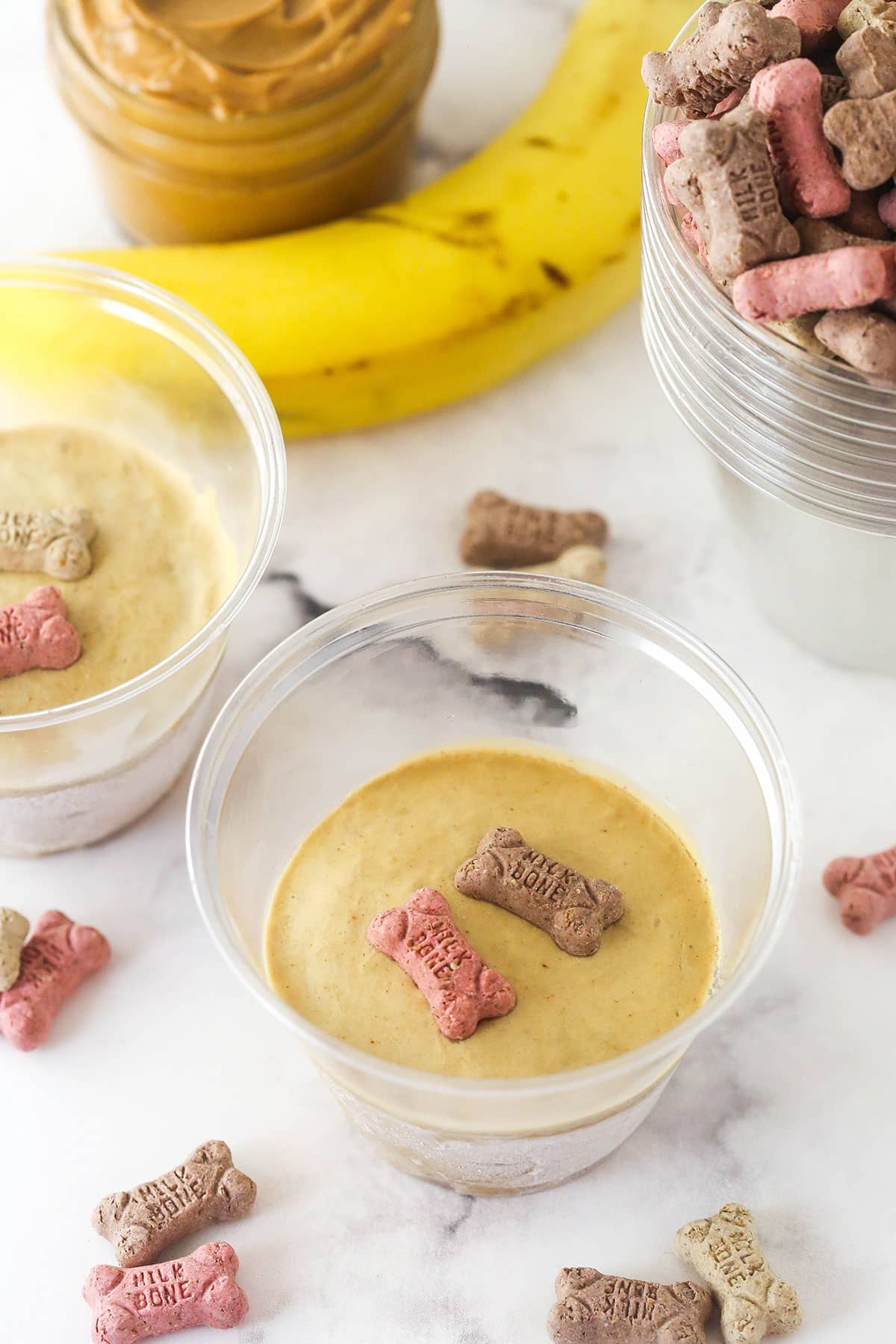These Peanut Butter Banana Frozen Dog Treats are made with 2 ingredients in less than 5 minutes. The perfect summer doggy treat! Overhead view of plastic cups of peanut butter banana frozen dog treats