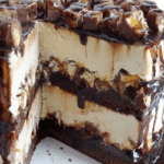 A Snickers Brownie Ice Cream Cake on a Cake Stand with a Slice Missing