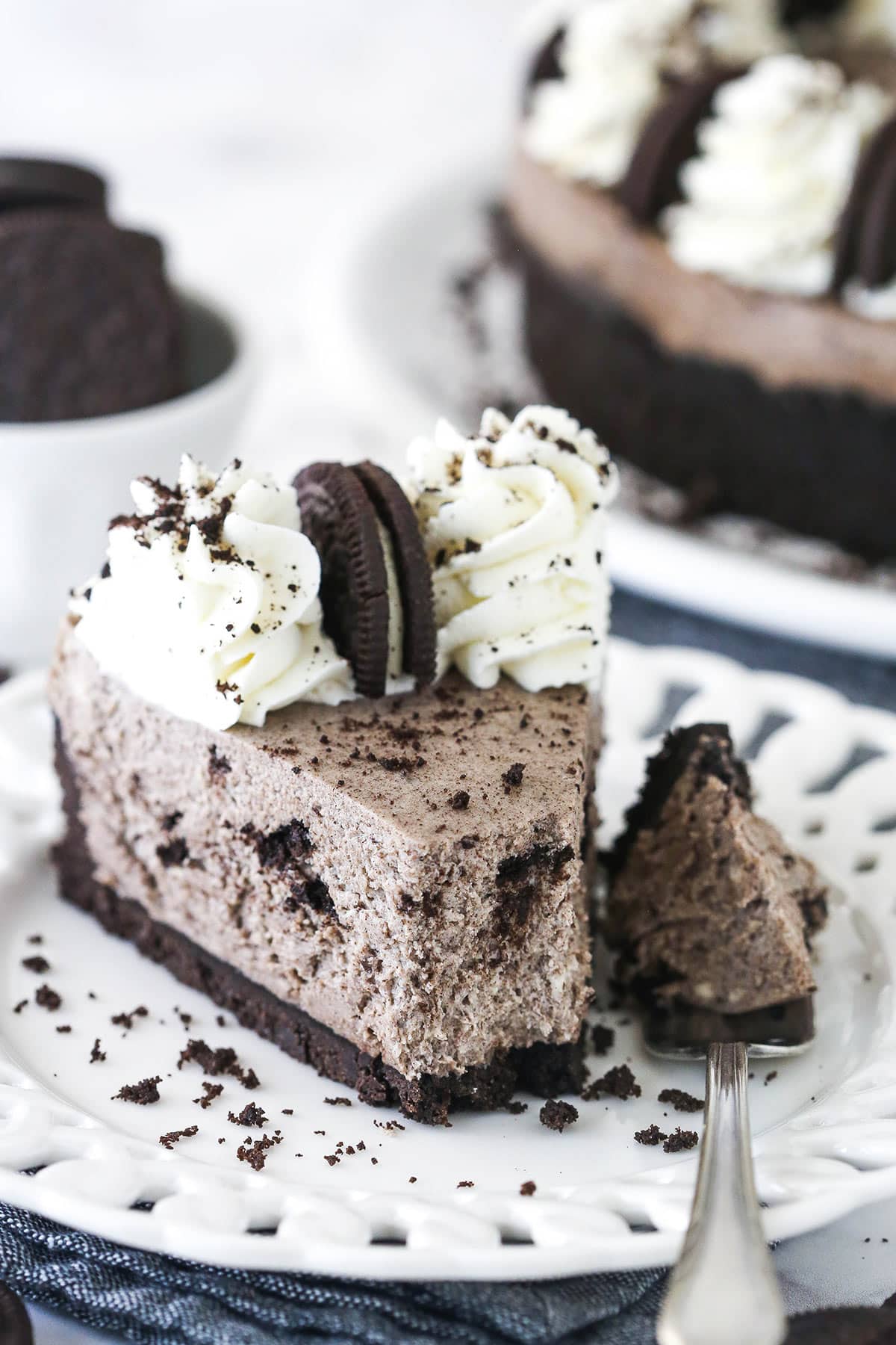 A slice of no bake oreo cheesecake on a white plate, a bite taken out.