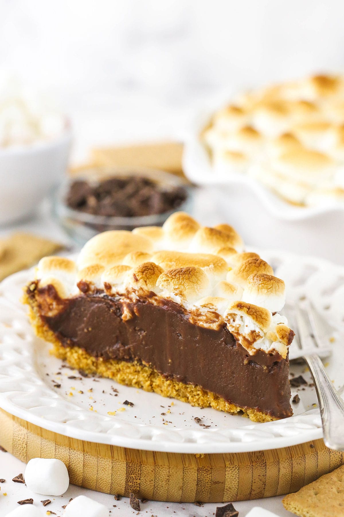 This S'mores Pie recipe has all the flavors you love from campfire s'mores! An easy chocolate pie topped with toasted marshmallows. A slice of smore's chocolate pie on a white plate