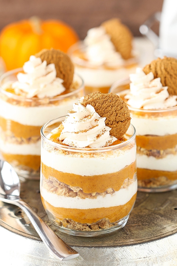 A sliver tray holding three mini pies and a metal spoon with a pumpkin in the background