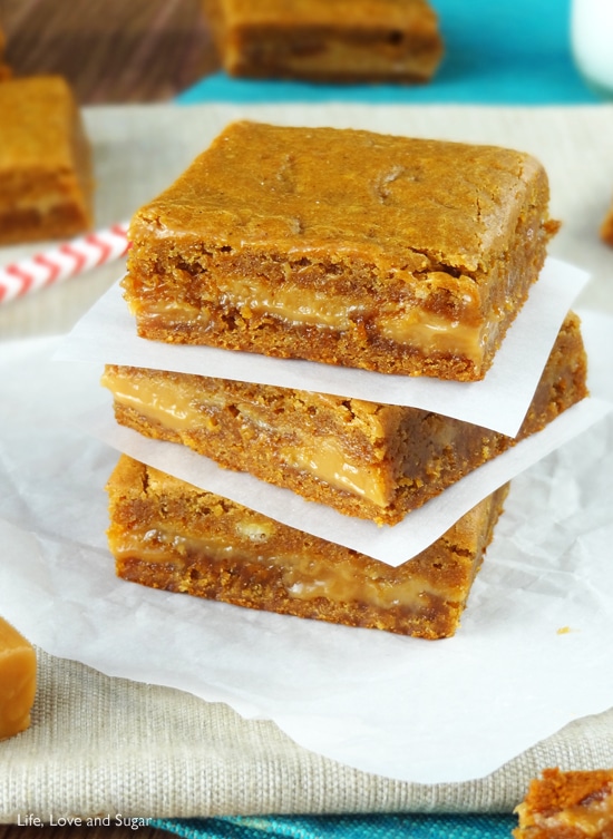 Three square Gingerbread Caramel Gooey Bars stacked on wax paper with more paper between each one