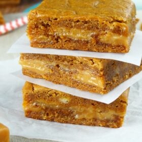 Three square Gingerbread Caramel Gooey Bars stacked on wax paper