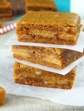 Three square Gingerbread Caramel Gooey Bars stacked on wax paper