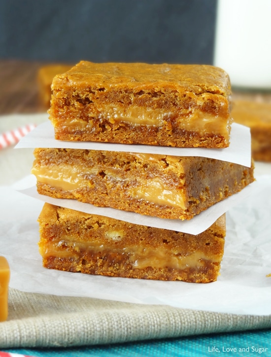 Three square Gingerbread Caramel Gooey Bars stacked on wax paper