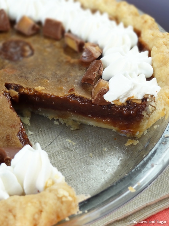 A Chocolate Hazelnut Chess Pie topped with Rolos and whipped cream has a slice missing