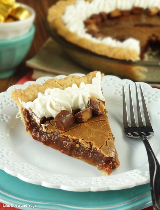 A slice of Chocolate Hazelnut Chess Pie with Rolos and whipped cream on top sits on a white plate with a fork