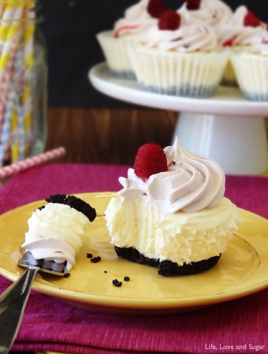 A Cheesecake Ice Cream Cupcake topped with whipped cream and a raspberry has a fork taking a piece out of it
