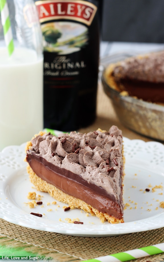 A slice of chocolate pie on a white plate with a bottle of Bailey behind it