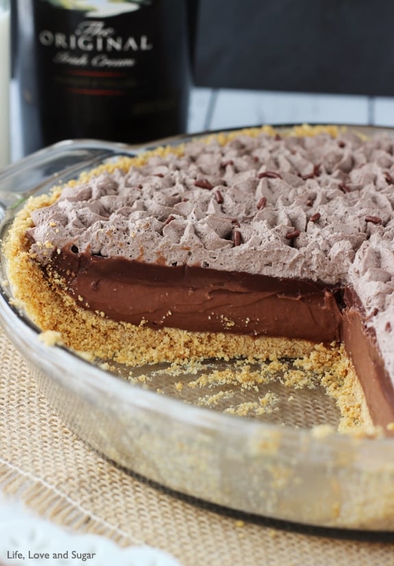 A glass dish filled with chocolate pie has a piece missing so you can see the layers of chocolate filling, ganache and whipped cream