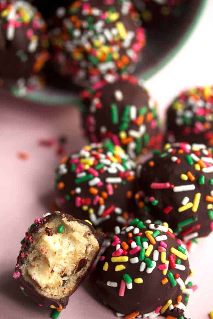 A pile of cheesecake chocolate chip cookie dough truffles with a bite take from one to show the center. 