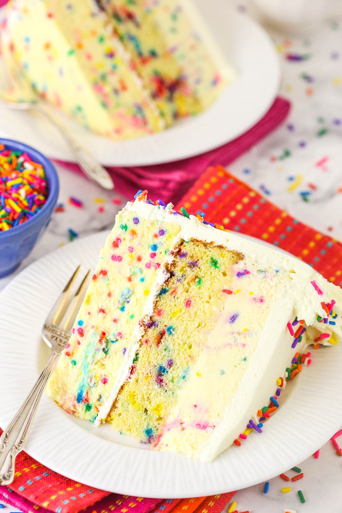 A slice of funfetti cake with cheesecake and mousse layers on a white plate