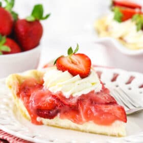 A piece of homemade berry pie on a plate with the remaining pie behind it