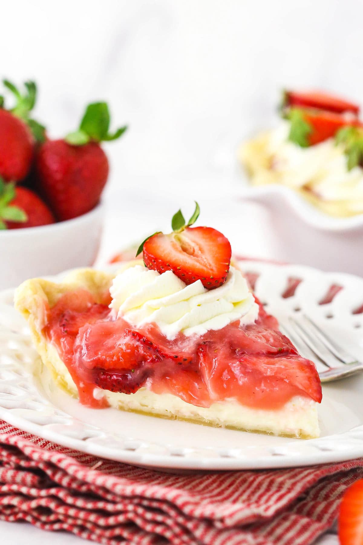 A piece of homemade berry pie on a plate with the remaining pie behind it