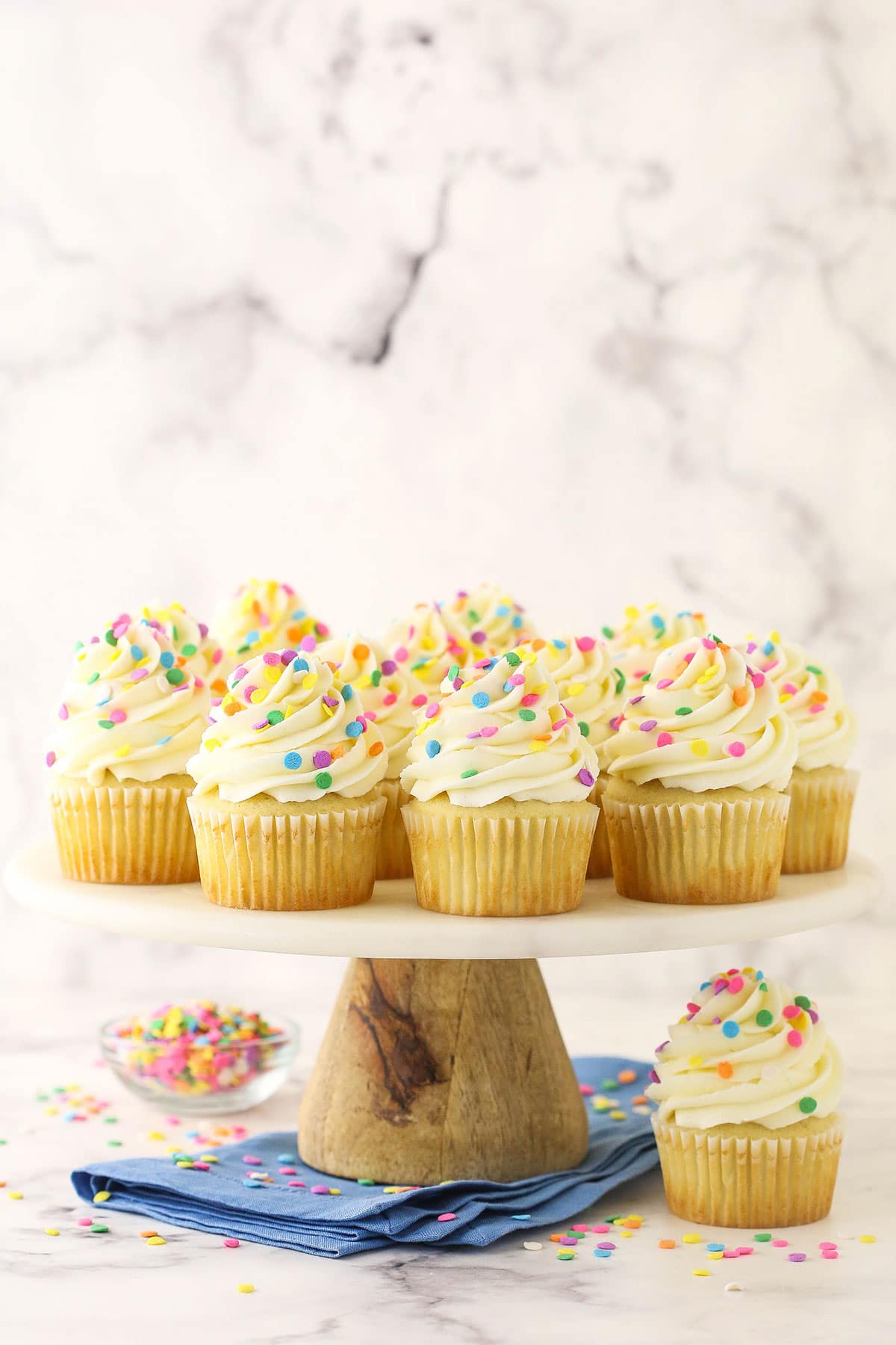 vanilla cupcakes on wood and marble cake stand with blue napkin underneath