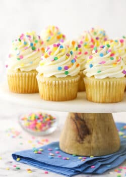vanilla cupcakes with multicolored sprinkles on wood and marble cake stand