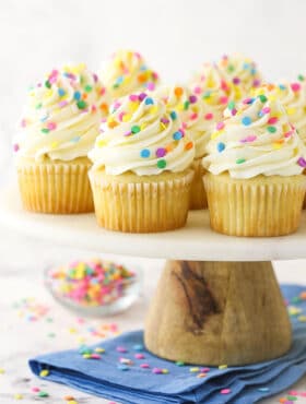 vanilla cupcakes with multicolored sprinkles on wood and marble cake stand