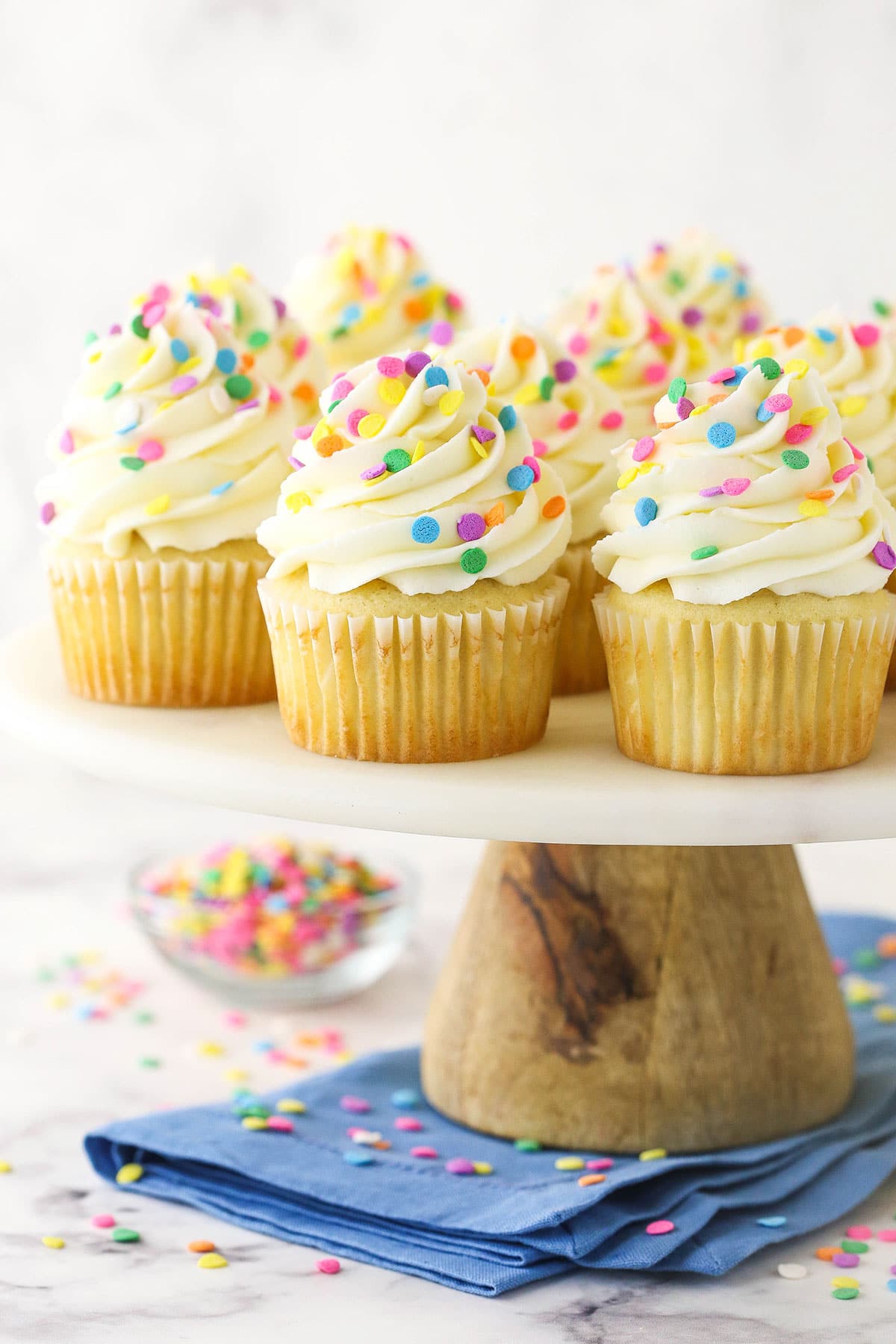 vanilla cupcakes with multicolored sprinkles on wood and marble cake stand