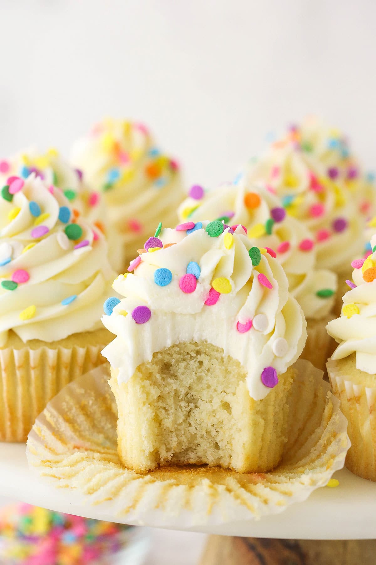 vanilla cupcake with a bite taken on a cake stand