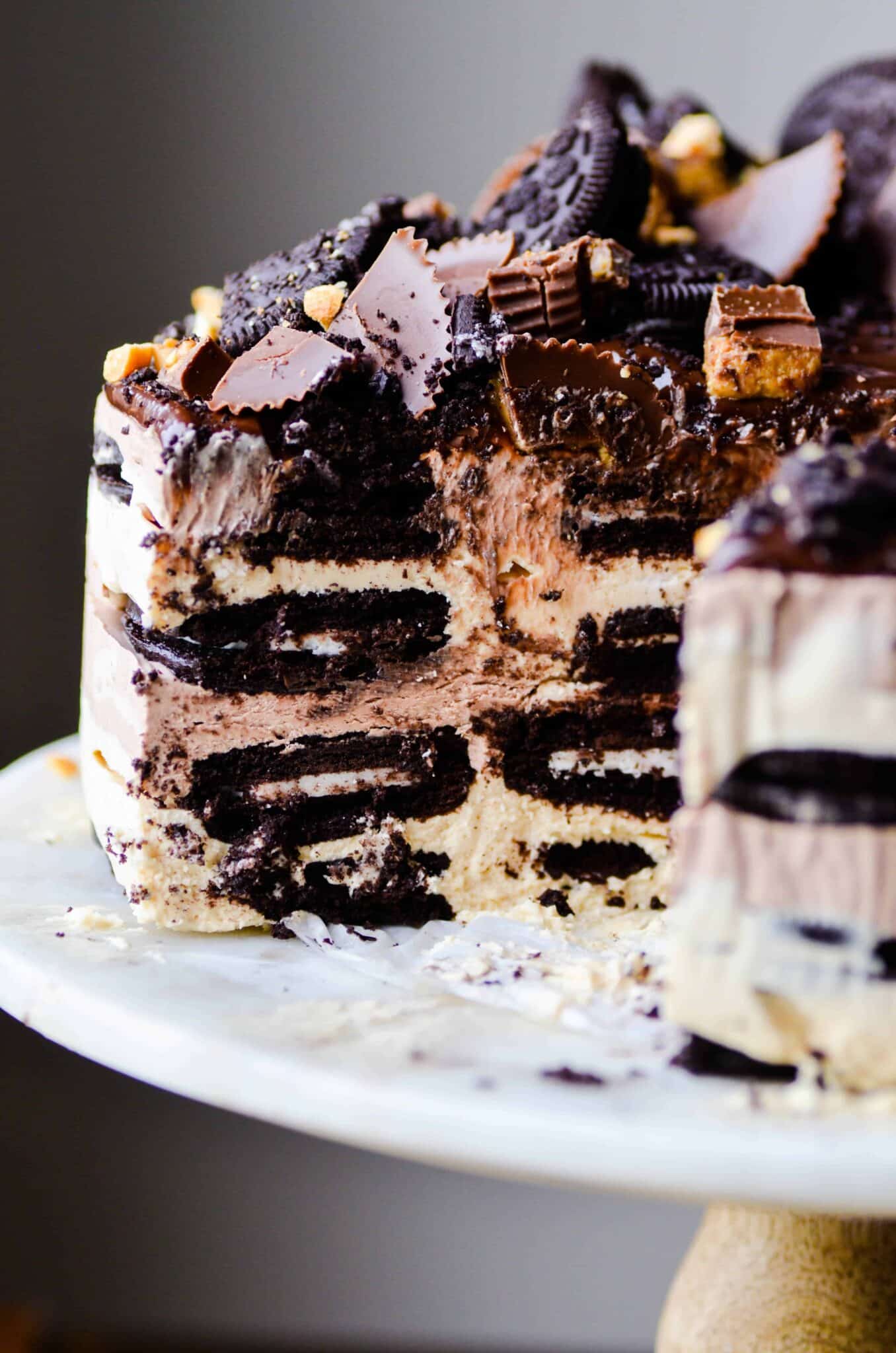 A Peanut Butter Oreo Icebox Cake on a cake plate with a few slices removed to show center layers of the cake.