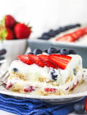 slice of berry icebox cake on white plate with blue napkin underneath and berries in the background
