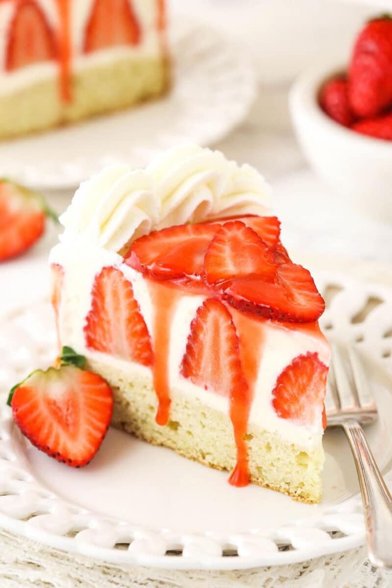 Strawberry Shortcake Cheesecake slice of strawberry shortcake cheesecake on white plate with sauce drizzling down